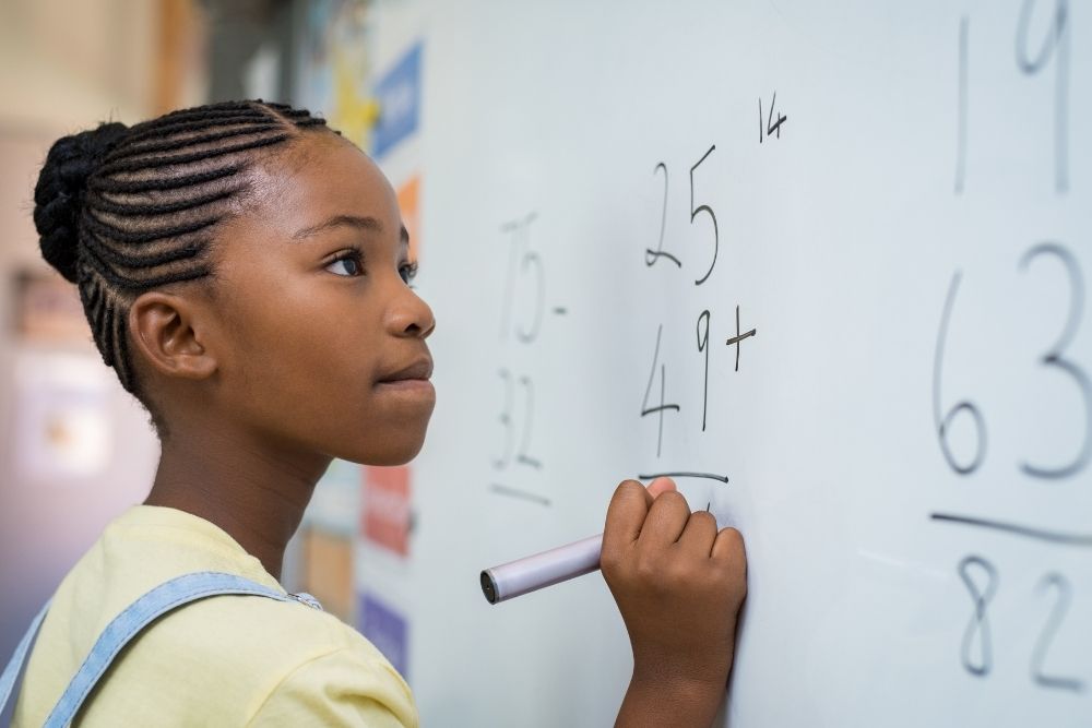 aluna resolvendo operação matemática no quadro branco.